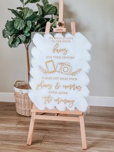 a white sign with gold lettering on it and a potted plant next to it