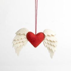 an ornament with white wings and a red heart hanging from a string on a white background