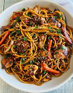 a white bowl filled with noodles and meat on top of a wooden table next to chopsticks