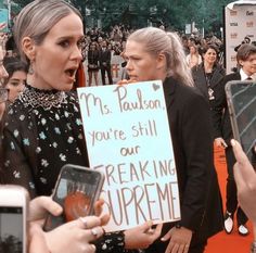 two women holding up signs and talking to each other while others take pictures with their cell phones