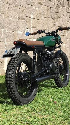 a green motorcycle parked in front of a brick wall with a wooden handlebar on it