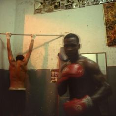 a man with boxing gloves on standing in front of a mirror and another person holding a punching bag