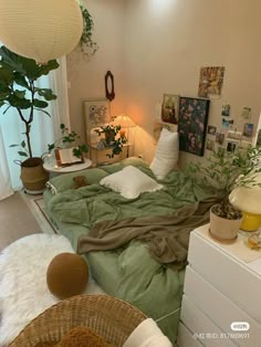 a bed with green sheets and pillows next to a plant in a room filled with pictures