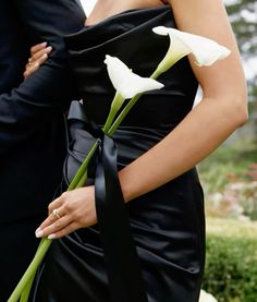 a woman in a black dress holding a white flower with her arm around the man's waist