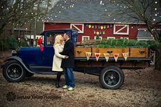 a man and woman standing next to an old truck with christmas trees on the back