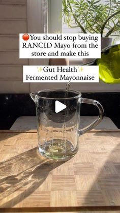 a glass pitcher filled with liquid sitting on top of a wooden table next to a plant