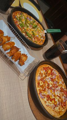 two pizzas and some chicken wings on a table