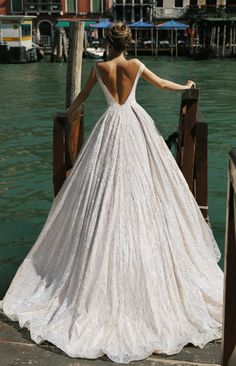 a woman in a white wedding dress standing on a pier looking at the water and buildings