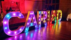 the letters are lit up with colorful lights in front of a wooden floor and wall