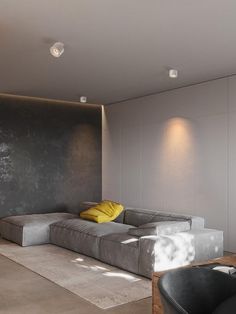 a living room filled with furniture next to a wall covered in concrete tiles and yellow pillows