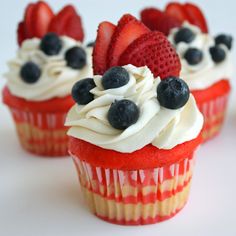 three cupcakes with strawberries and blueberries on top are sitting next to each other