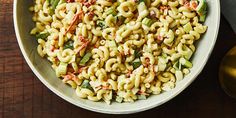 a white bowl filled with macaroni salad on top of a wooden table next to a knife