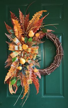 a wreath with oranges and green leaves hanging on a front door, next to a green door