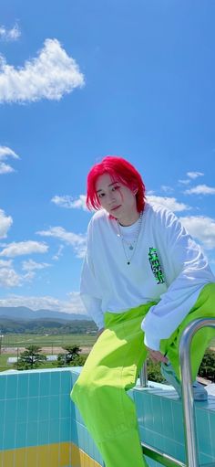 a woman with red hair sitting on top of a metal railing next to a swimming pool