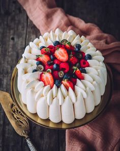 a white cake with strawberries and blueberries on top sits on a gold plate