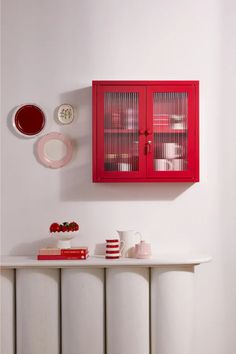 a red cabinet on the wall above a white radiator with plates and cups