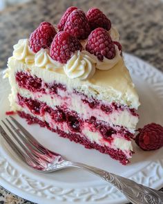 a piece of cake with raspberries and cream frosting on a white plate