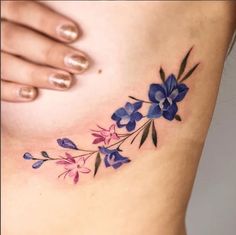 a woman's stomach with blue and pink flowers on the side, tattoo style