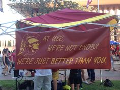 a group of people standing under a tent with a sign that says at usc, we're not shops were just better than you