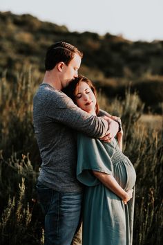 a pregnant woman hugging her husband in a field