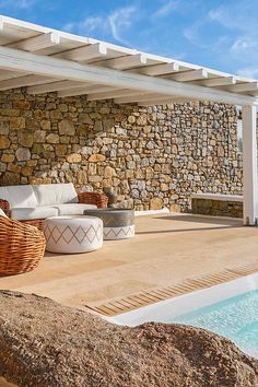 an outdoor living area with wicker furniture next to a swimming pool and stone wall