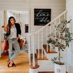 a woman standing in front of a stair case holding a handbag next to a potted plant