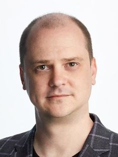 a man with a bald head wearing a black and white shirt is looking at the camera