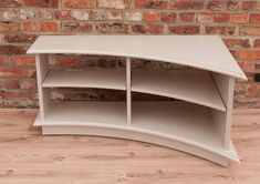 a curved shelf sitting on top of a hard wood floor next to a brick wall