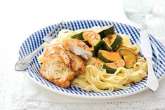 a plate with chicken, zucchini and squash on it next to a glass of water