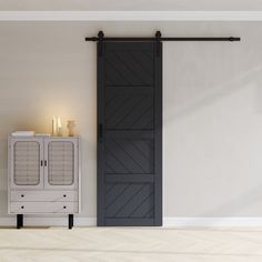 an empty room with a white cabinet and black barn door next to a lit candle