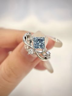 a woman's hand holding an engagement ring with blue and white diamonds