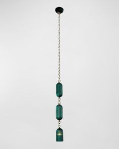 three green glass beads hanging from a metal chain on a white wall with a black light fixture in the background