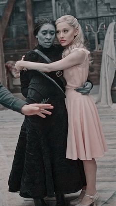 two people dressed in black and pink hugging each other on the street while one person is holding another woman's arm