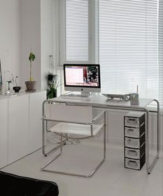 a white desk with a computer on it in front of a window and some drawers