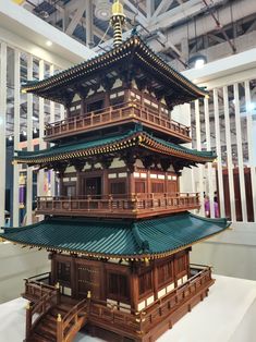 a tall wooden building with green roofing and white columns on the top floor in an indoor area