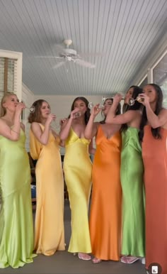 four women in long dresses are holding wine glasses up to their mouths as they look at each other