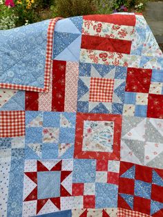 a red, white and blue quilt is laying on the ground next to some flowers