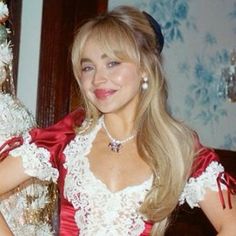 a woman in a red and white dress standing next to a christmas tree