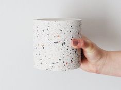 a hand holding a white cup with speckles on it