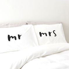 two pillows with mr and mrs written on them in black ink sitting on a bed