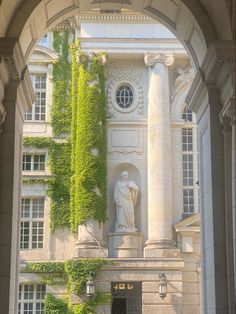 an archway with ivy growing on the side of it and statues at the top, in front of a building