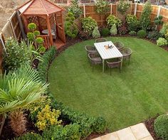 a table and chairs are in the middle of a garden with green grass, shrubs and trees