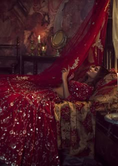 a woman is laying in bed with a red canopy over her head and holding a lit candle