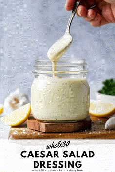 a person dipping dressing into a jar with lemon wedges