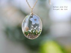 a necklace with flowers and grass inside it on a chain that says ashes and fur forgets, forget me not