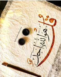 an arabic calligraphy is displayed on a piece of parchment paper with two black buttons