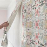 a woman is painting the wall with paint rollers in her home, and she's holding on to the curtain