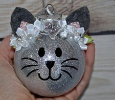 a hand holding an ornament with a cat face on it