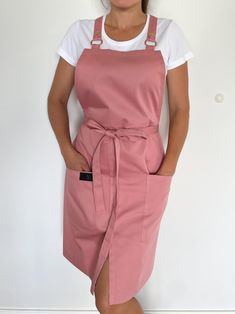 a woman wearing an apron standing in front of a white wall with her hands on her hips