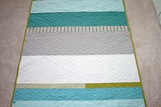 a blue and white striped quilt on the floor next to a rug with green trim